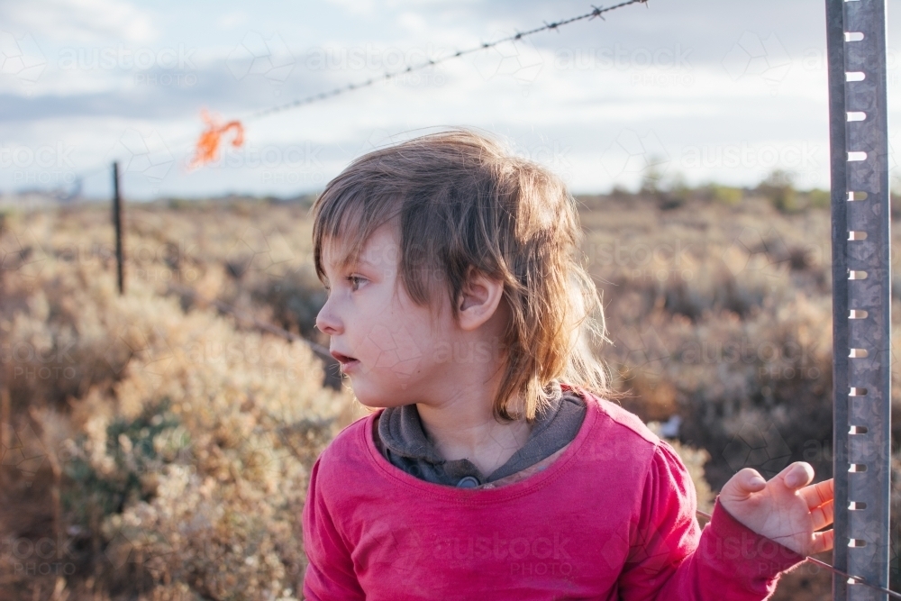 Young girl standing by barbwire fence - Australian Stock Image