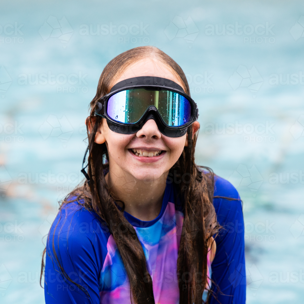 Young girl standing in a swimming pool wearing a rash guard and large reflective goggles - Australian Stock Image