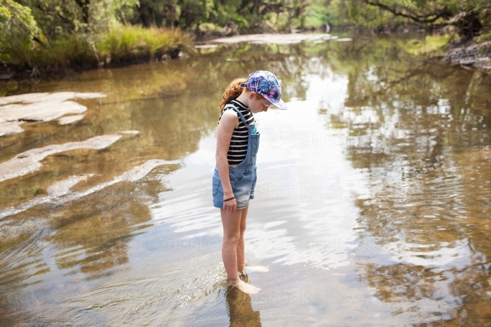 Young girl standing in the river looking down - Australian Stock Image