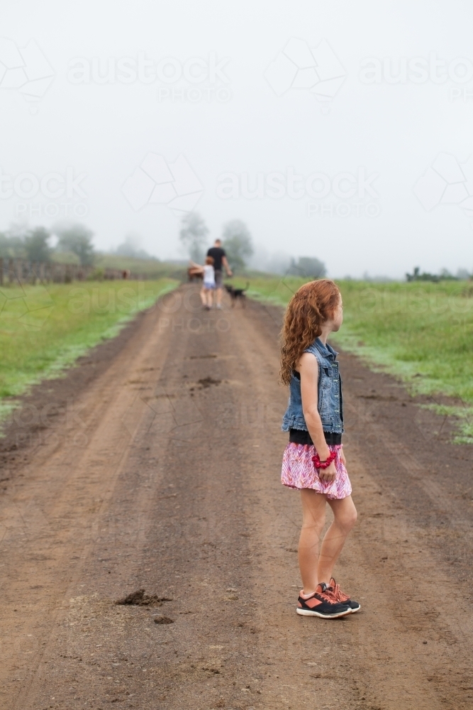 Young girl standing on a dirt track with family in the distance - Australian Stock Image