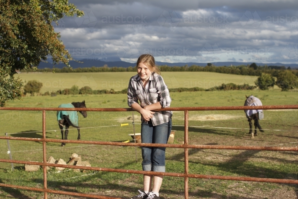 Young girl standing on a fence at a horse riding farm - Australian Stock Image