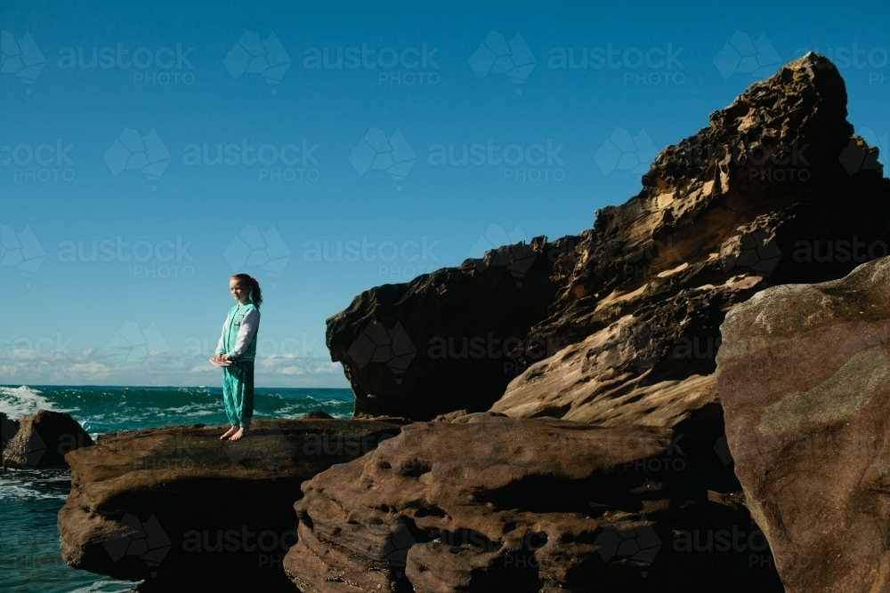 Young girl standing on a rock at the beach - Australian Stock Image