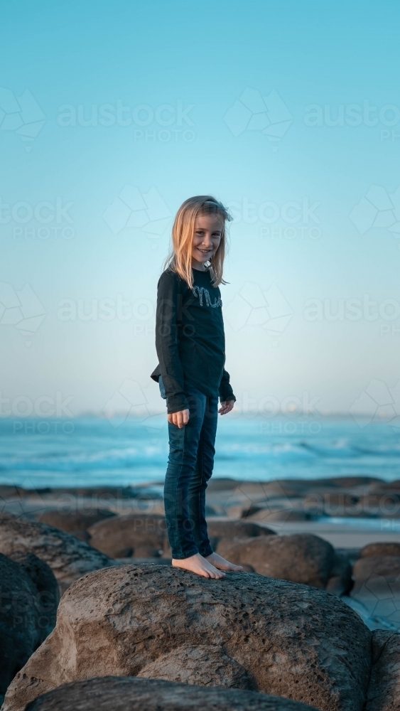 Young girl standing on rock at the beach - Australian Stock Image