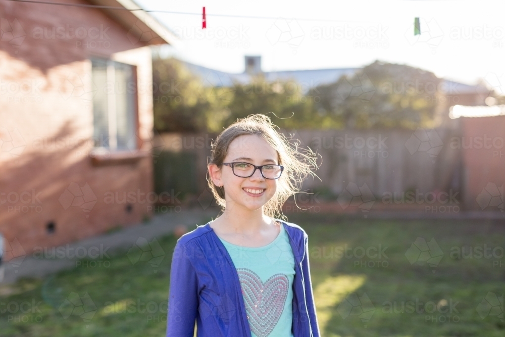 Young girl standing under washing line smiling - Australian Stock Image