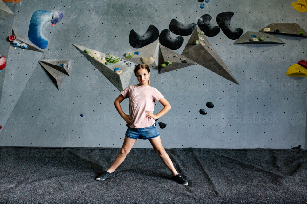 Young girl standing with legs wide open on the crash pad in an indoor rock-climbing gym. - Australian Stock Image