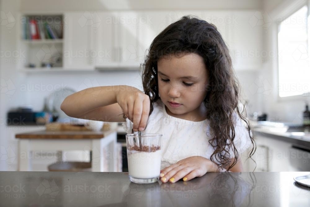 Young girl stirring chocolate into a glass of milk - Australian Stock Image