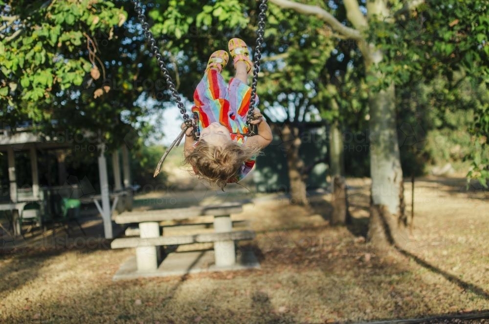 Young girl swinging high on swings at playground - Australian Stock Image
