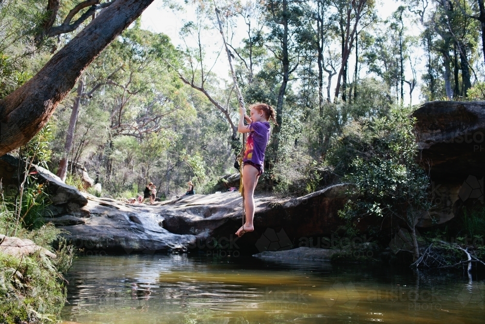 Young girl swinging on a rope swing at a waterhole - Australian Stock Image