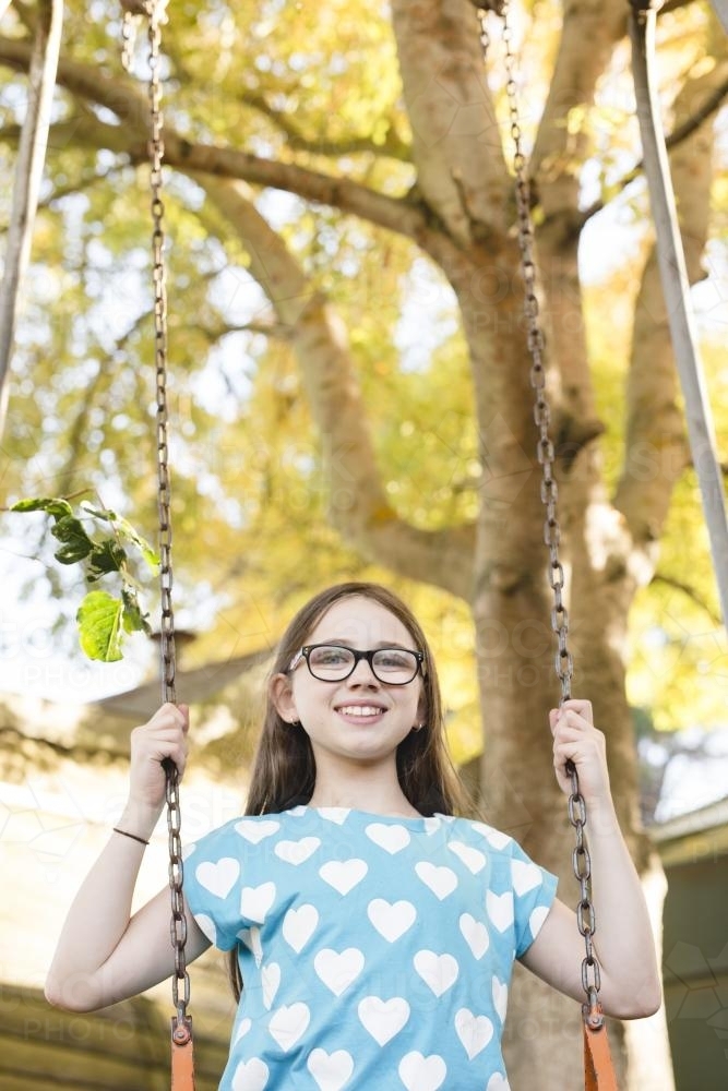 Young girl swinging on backyard swing in golden light - Australian Stock Image