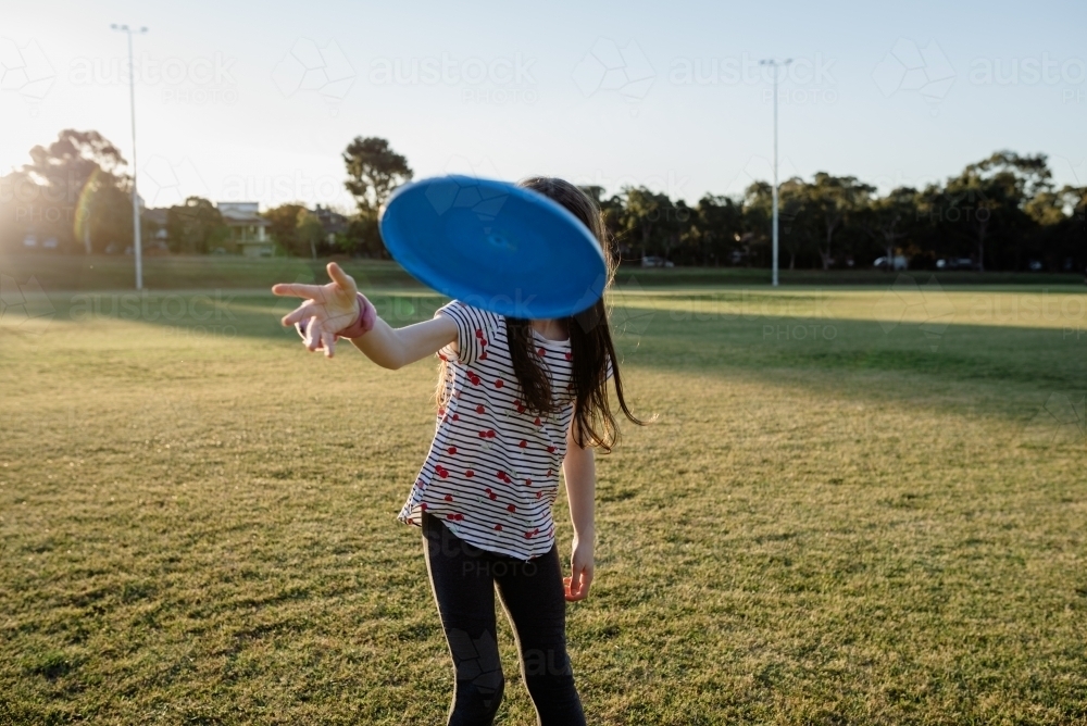 Young girl throwing a flying disk / frisbee at a sports field (oval) at sunset - Australian Stock Image
