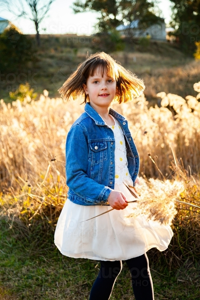 Young girl twirling around outside backlit by golden light - Australian Stock Image