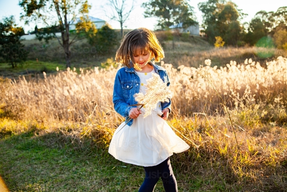 Young girl twirling around outside backlit by golden light - Australian Stock Image