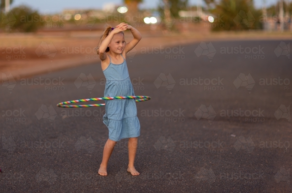 young girl twirling hula hoop around waist in evening light - Australian Stock Image