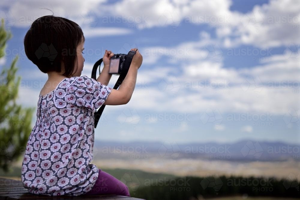 Young girl using a camera whilst on holiday to take a photo of a valley - Australian Stock Image