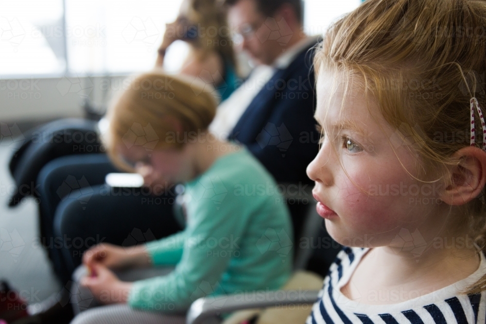 Young girl waiting at the departure lounge of an airport with other people in the background - Australian Stock Image