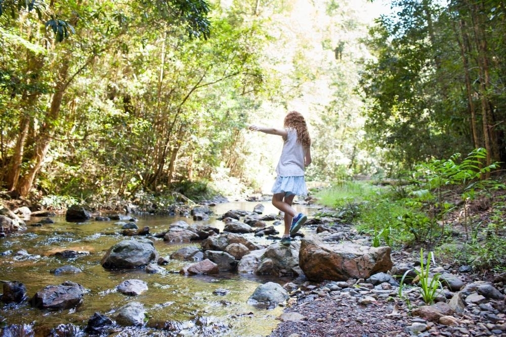 Young girl, walking across rocks at a creek - Australian Stock Image