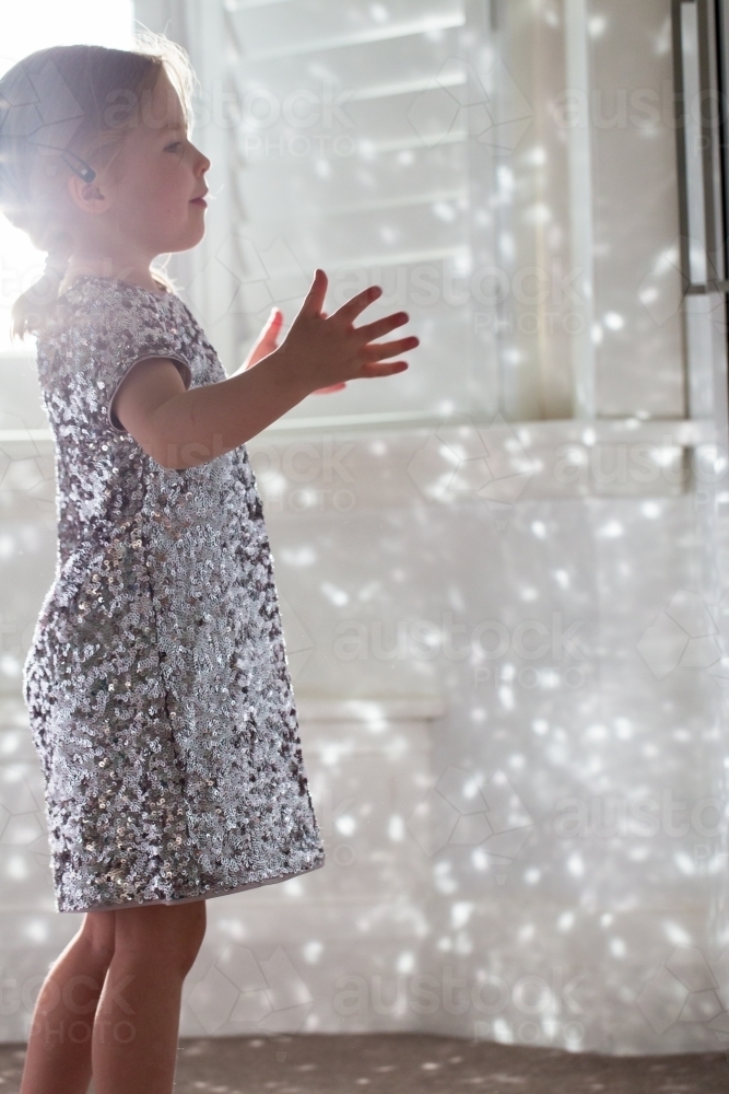 Young girl wearing a sparkly dress playing with the reflected light - Australian Stock Image