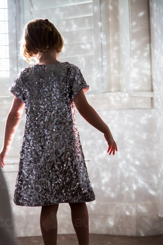 Young girl wearing a sparkly dress playing with the reflected light - Australian Stock Image