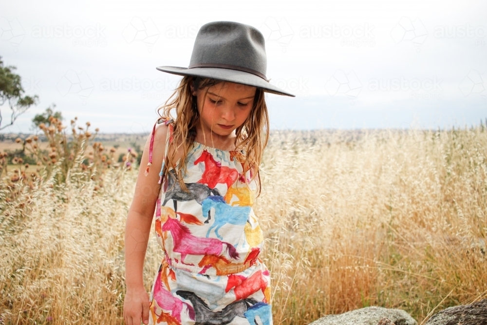 Young girl wearing grey bushman's hat in grassy fields - Australian Stock Image