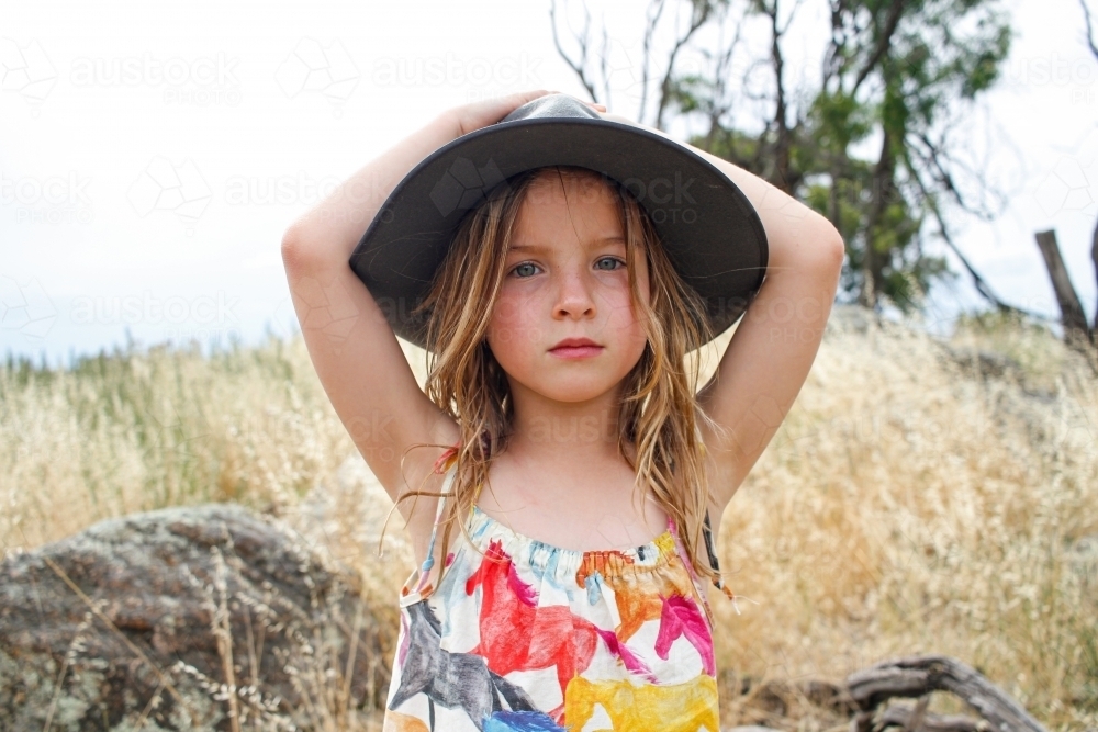 Young girl wearing grey bushman's hat in grassy fields - Australian Stock Image
