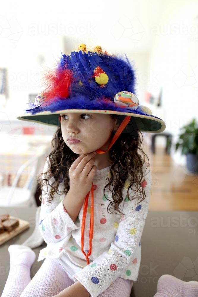 Young girl wearing hand made blue easter hat frowning - Australian Stock Image