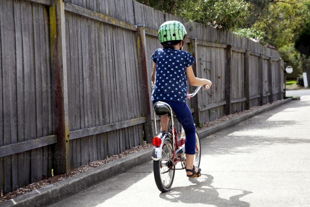 Young girl wearing helmet riding bike from behind - Australian Stock Image