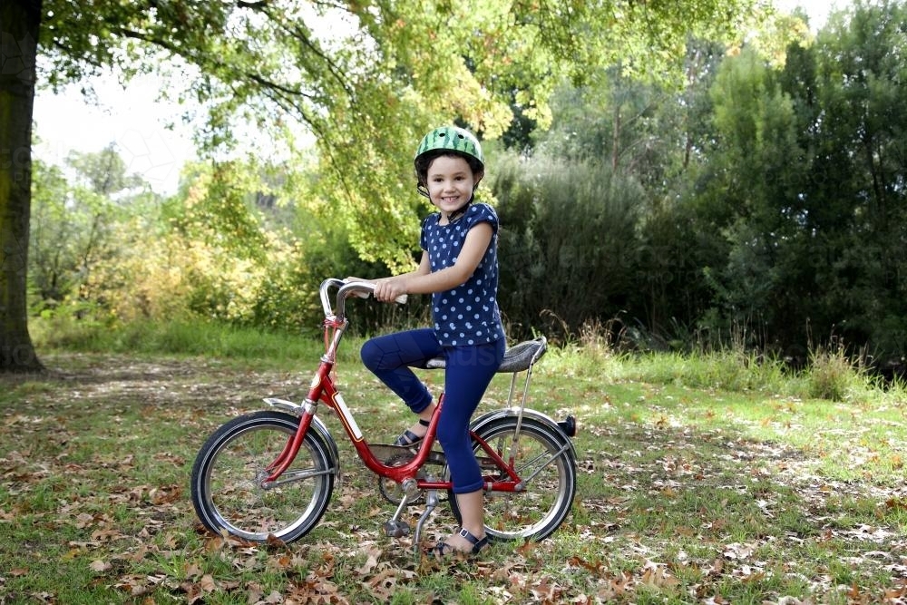 Young girl wearing helmet riding red bike - Australian Stock Image