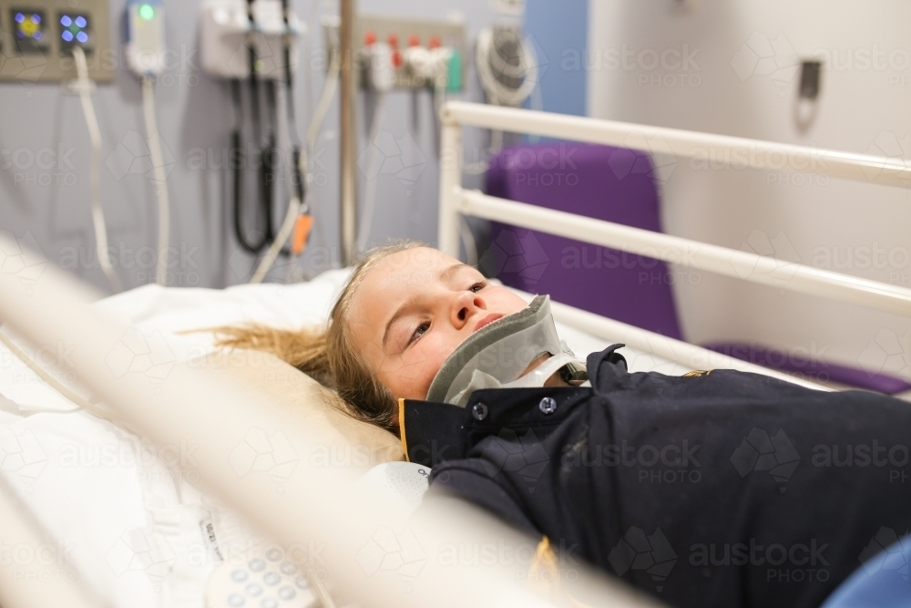 Young girl wearing neck brace in hospital bed - Australian Stock Image
