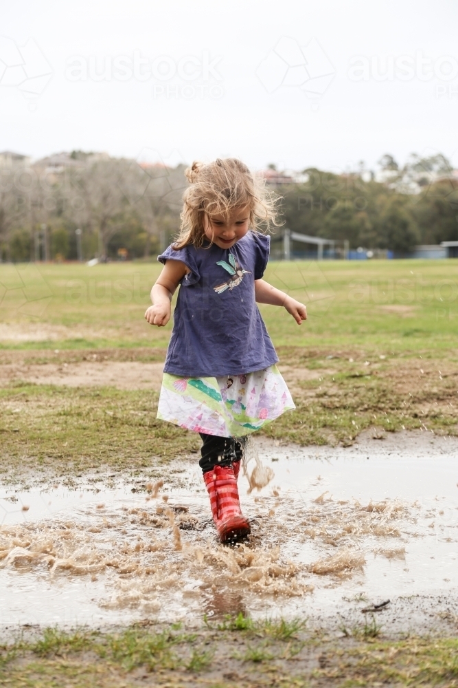 Young girl wearing red gumboots playing in puddles - Australian Stock Image