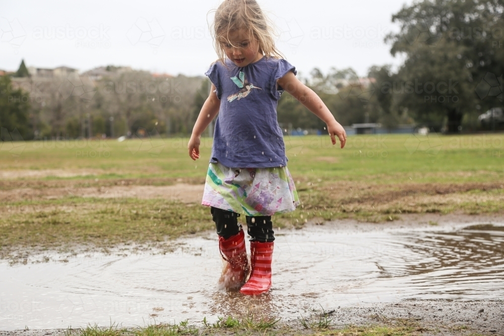 Young girl wearing red gumboots playing in puddles - Australian Stock Image