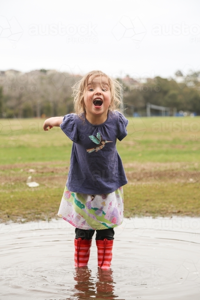 Young girl wearing red gumboots playing in puddles - Australian Stock Image