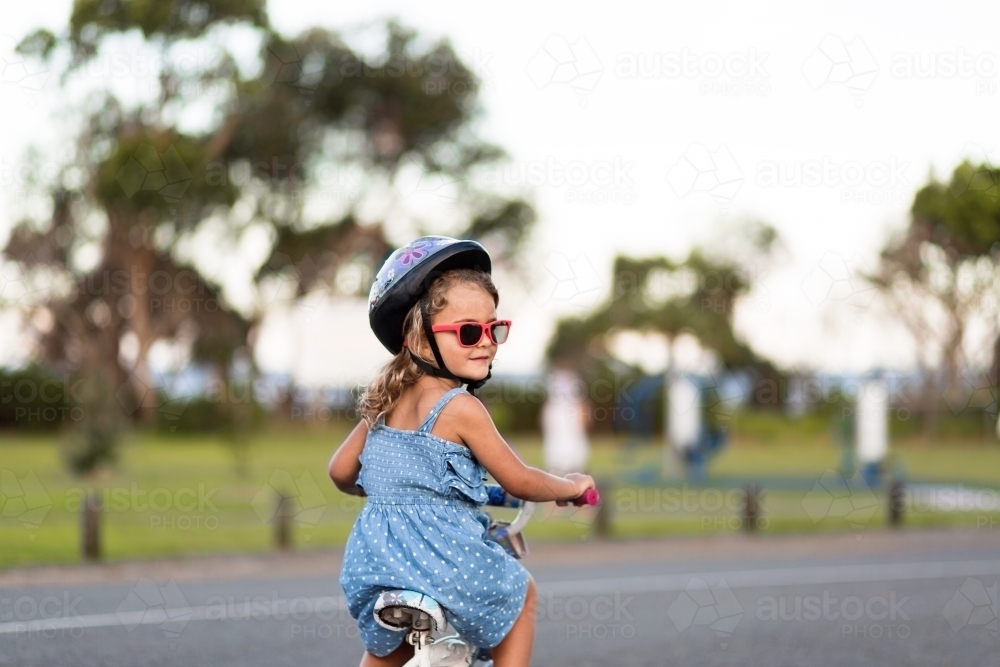 Young girl wearing sunglasses riding a bike - Australian Stock Image