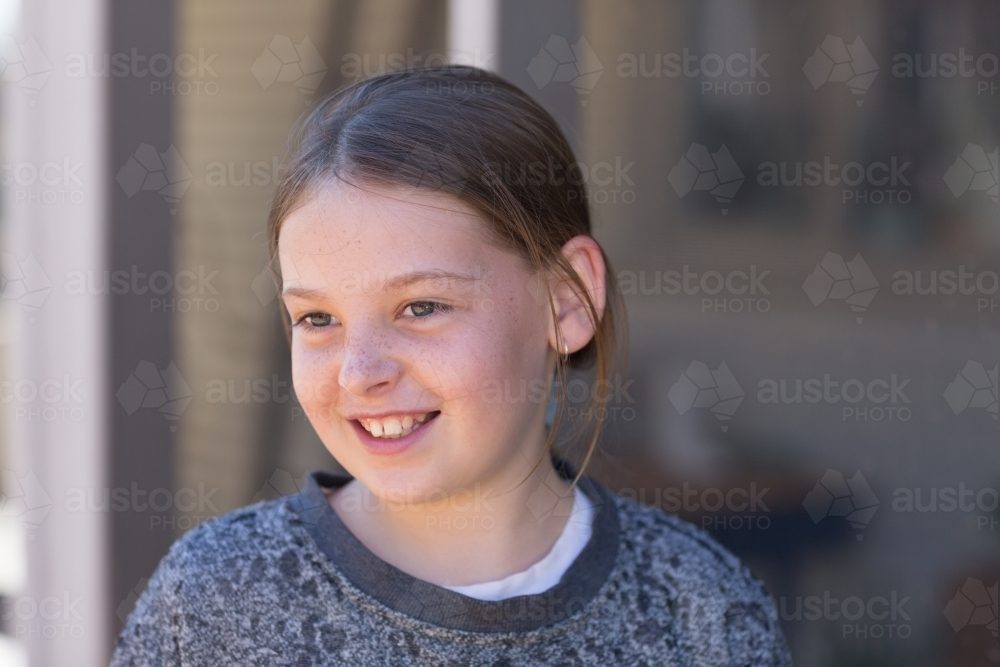 Young girl wearing sweater smiling while looking away - Australian Stock Image