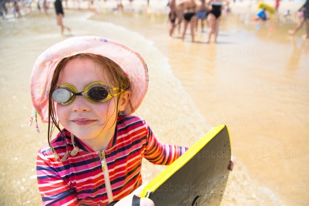 Young girl with a boogie board, goggles and hat at the beach - Australian Stock Image