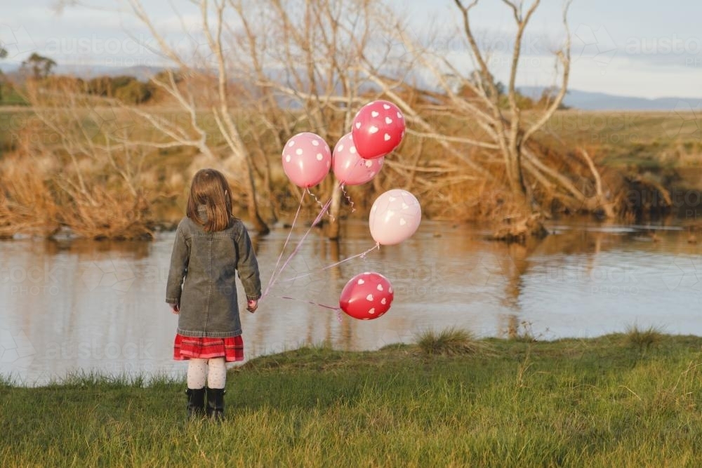 Young girl with a bunch of pink birthday balloons beside a river - Australian Stock Image