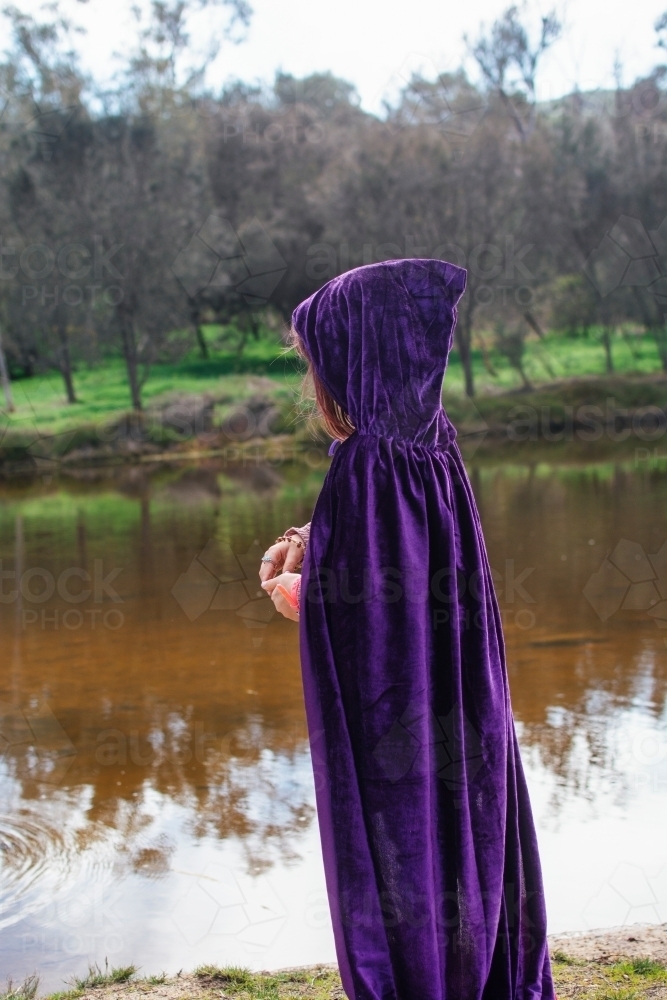 Young girl with a purple cape playing by river - Australian Stock Image