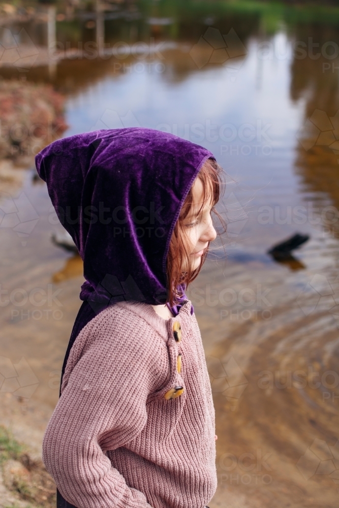 Young girl with a purple cape playing by river - Australian Stock Image