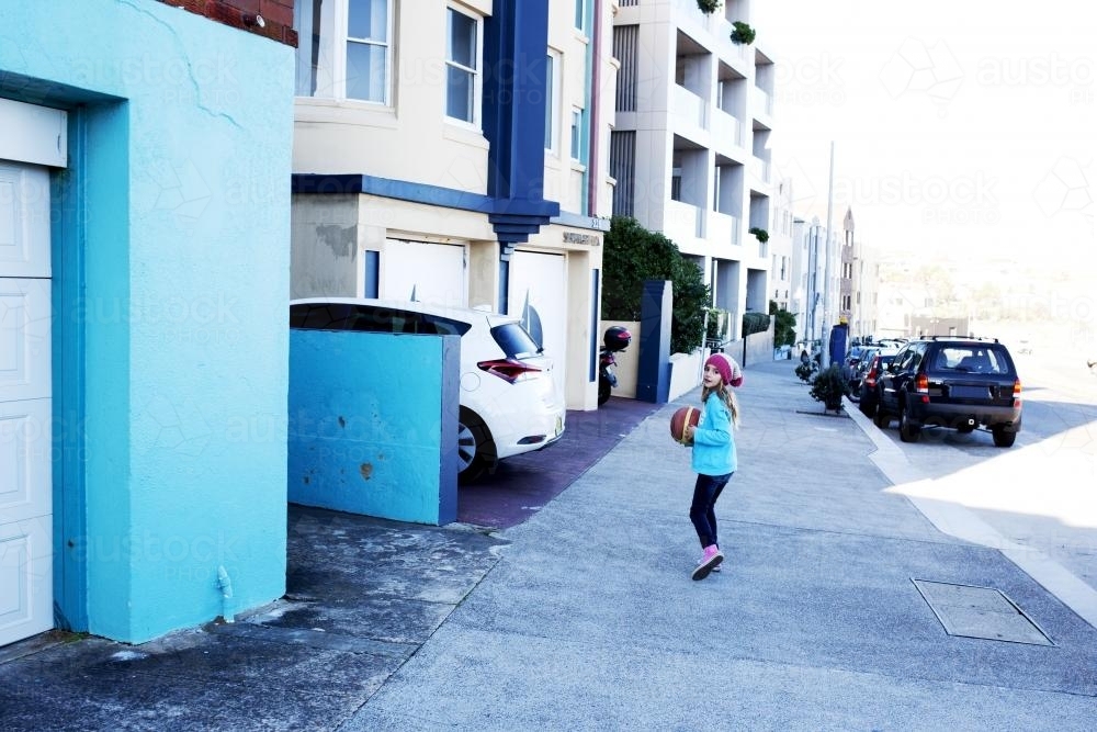 Young girl with basketball running down a blue street - Australian Stock Image