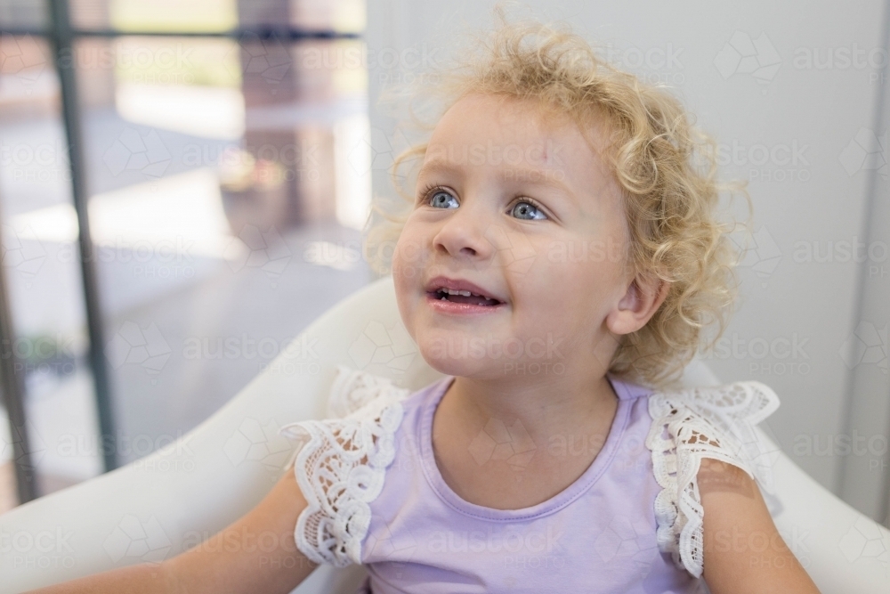 Young girl with blonde curls sitting in chair - Australian Stock Image