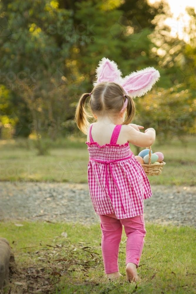 Young girl with bunny ears carrying a basket of Easter eggs - Australian Stock Image
