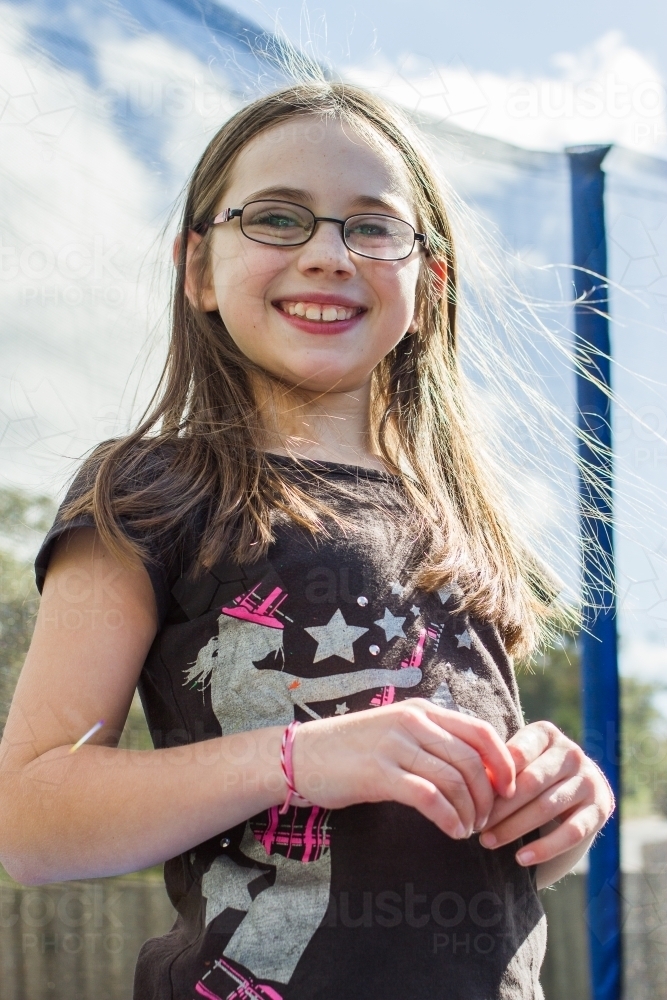 Young girl with glasses standing on trampoline smiling - Australian Stock Image