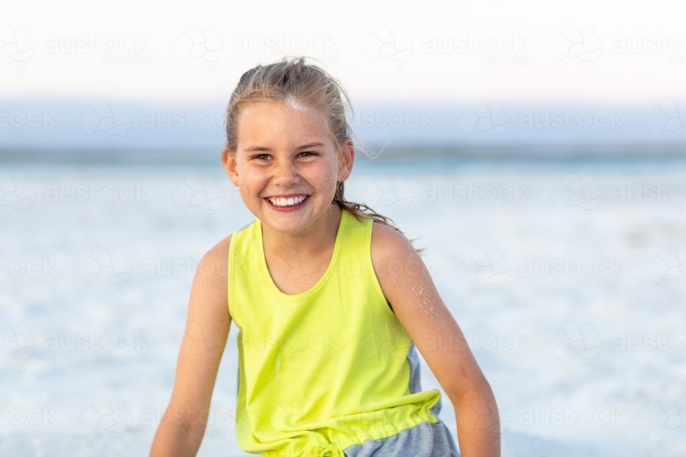 young girl with hair tied back in fluoro top on the beach - Australian Stock Image