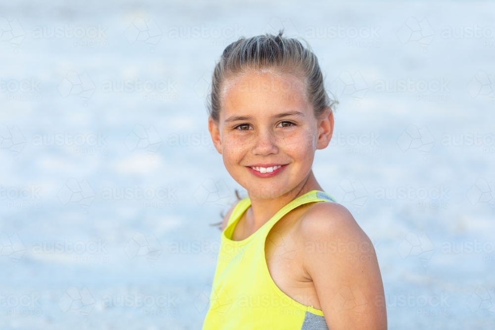 young girl with hair tied back in fluoro top on the beach - Australian Stock Image