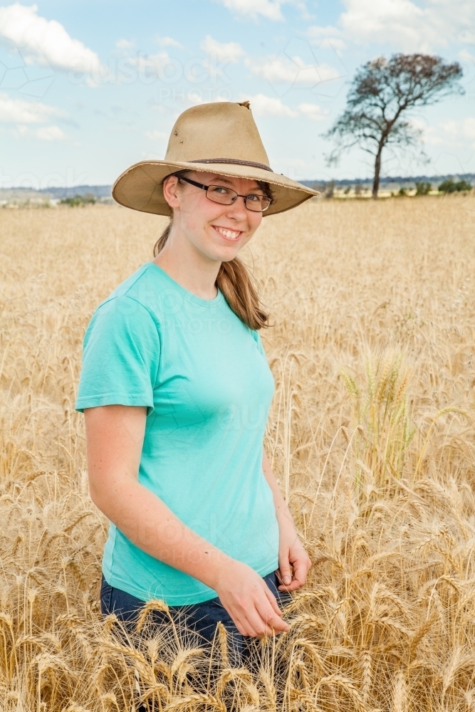 Image of Young girl with hat on standing in paddock of bearded wheat ...