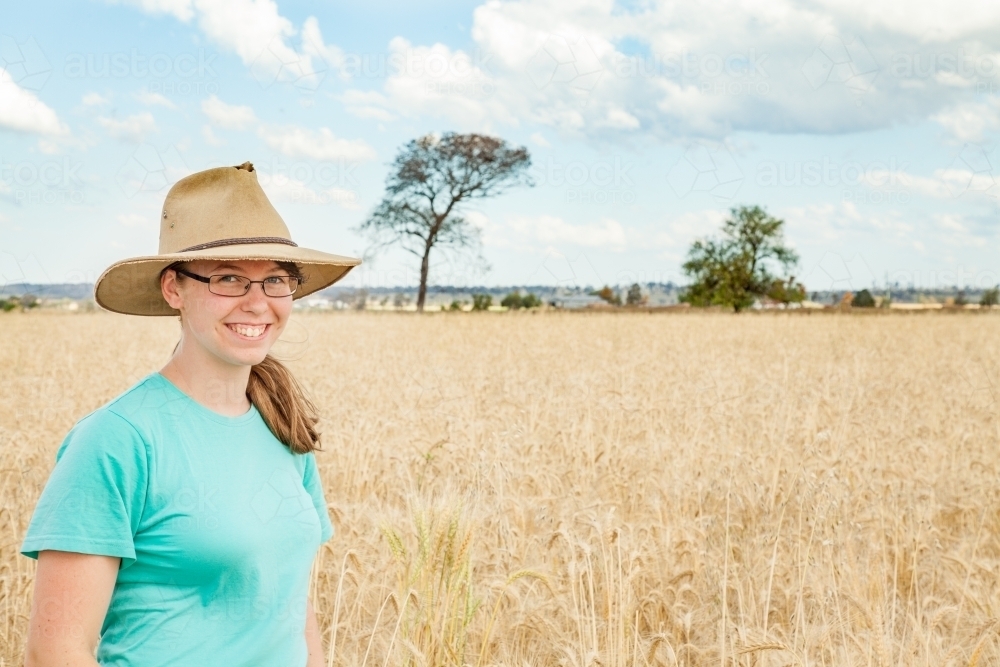 Young girl with hat on standing in paddock of bearded wheat crop on a farm - Australian Stock Image