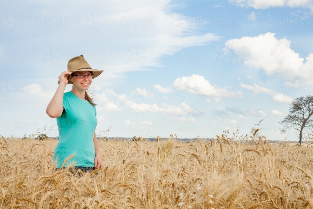 Young girl with hat on standing in paddock of bearded wheat crop on a farm - Australian Stock Image