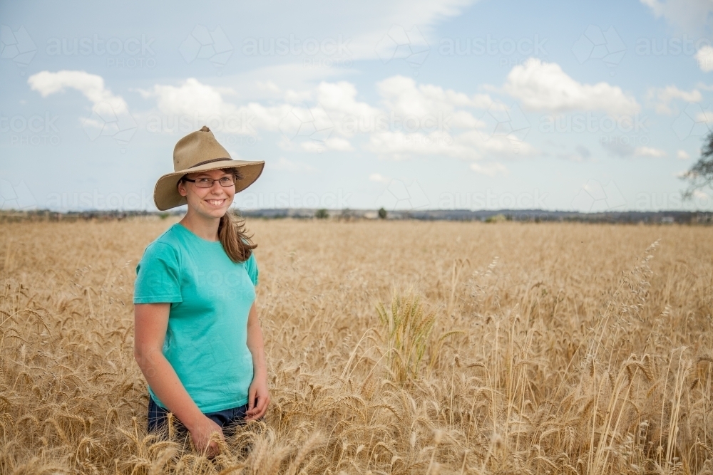 Young girl with hat on standing in paddock of bearded wheat crop on a farm - Australian Stock Image