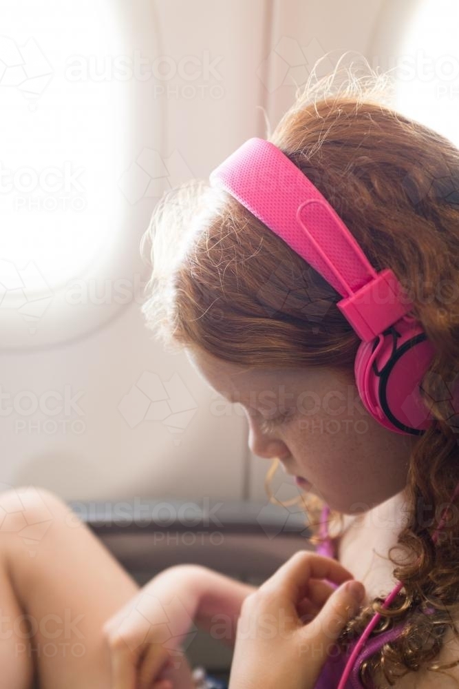 Young girl with headphones on a passenger plane - Australian Stock Image