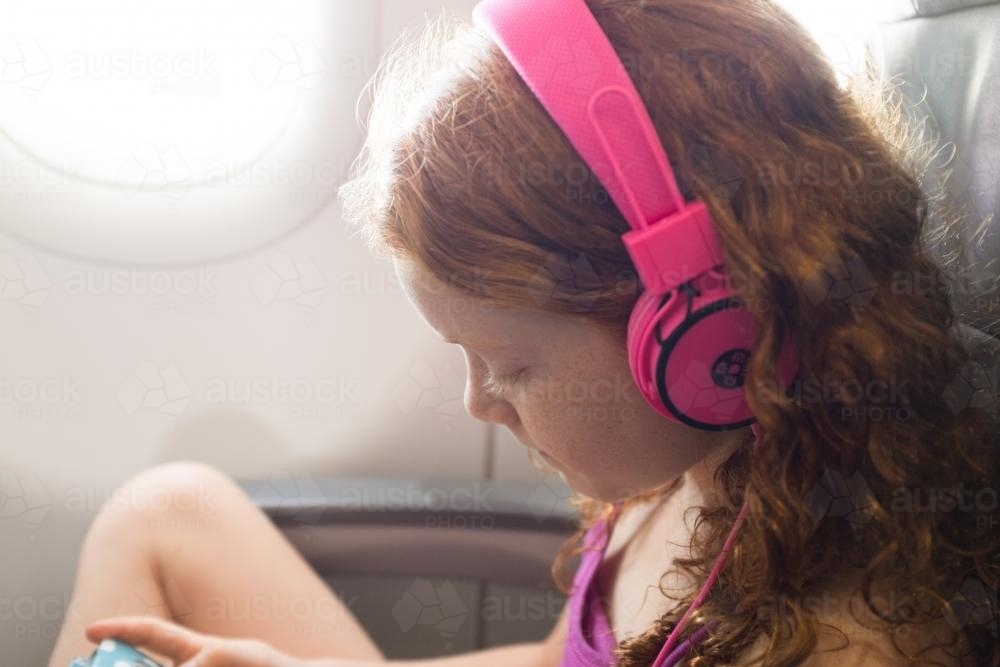 Young girl with headphones on a passenger plane - Australian Stock Image