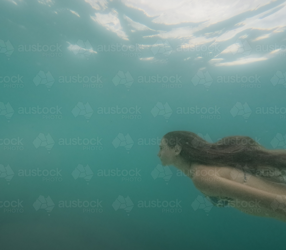 Young Girl with long hair swimming through green ocean water taken underwater - Australian Stock Image